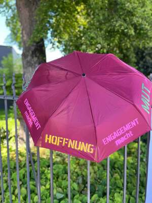 Bunt bespruehter Schirm mit der Aufschrift Engagement macht Hoffnung