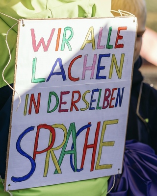 Demoschild mit der Aufschrift: Wir lachen alle in derselben Sparche
